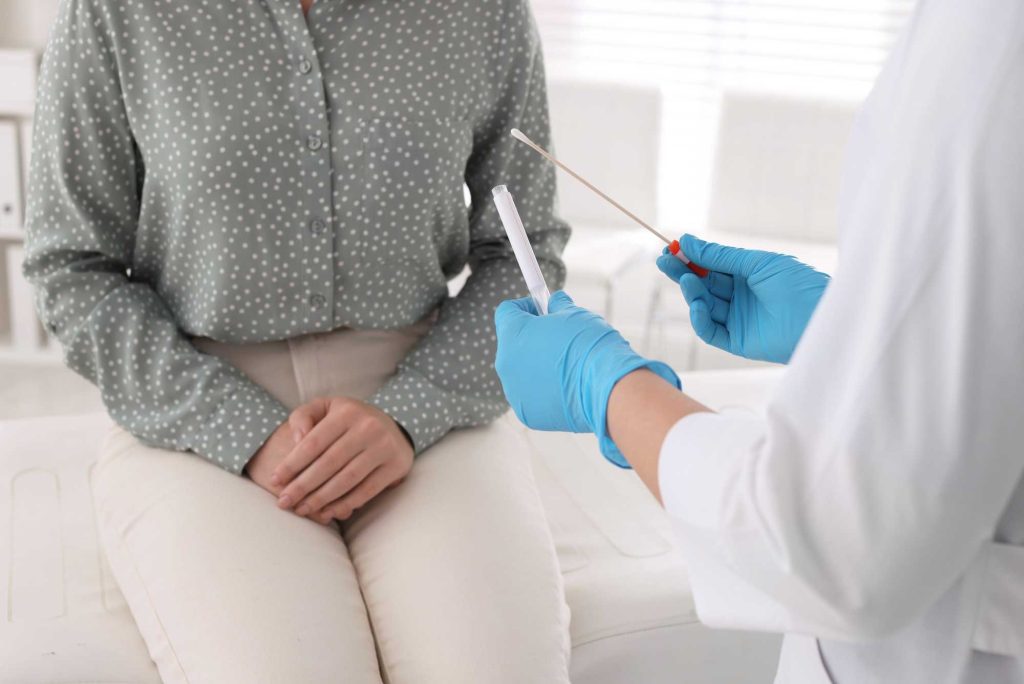 Close up of a doctor in an STD clinic holding a medical swab and test tube while consulting with a female patient.