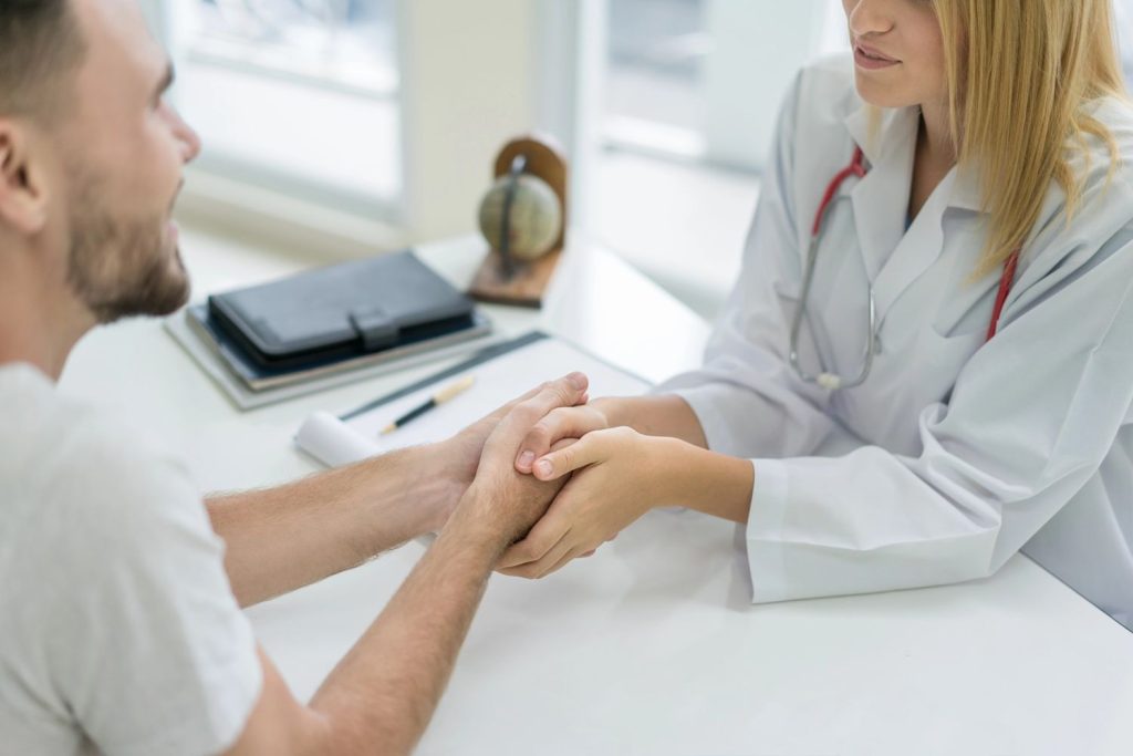 A compassionate doctor holding a male patient's hand during a supportive medical consultation at a local sti clinic.