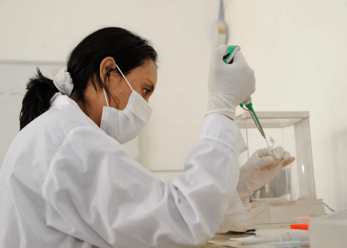A lab technician performs confidential std testing houston by pipetting a sample into a tube in a sterile medical lab.