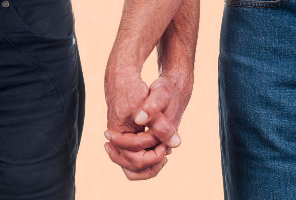 A close-up of two men’s linked hands, symbolizing relationship health and the results of a gay men STD test in Houston.