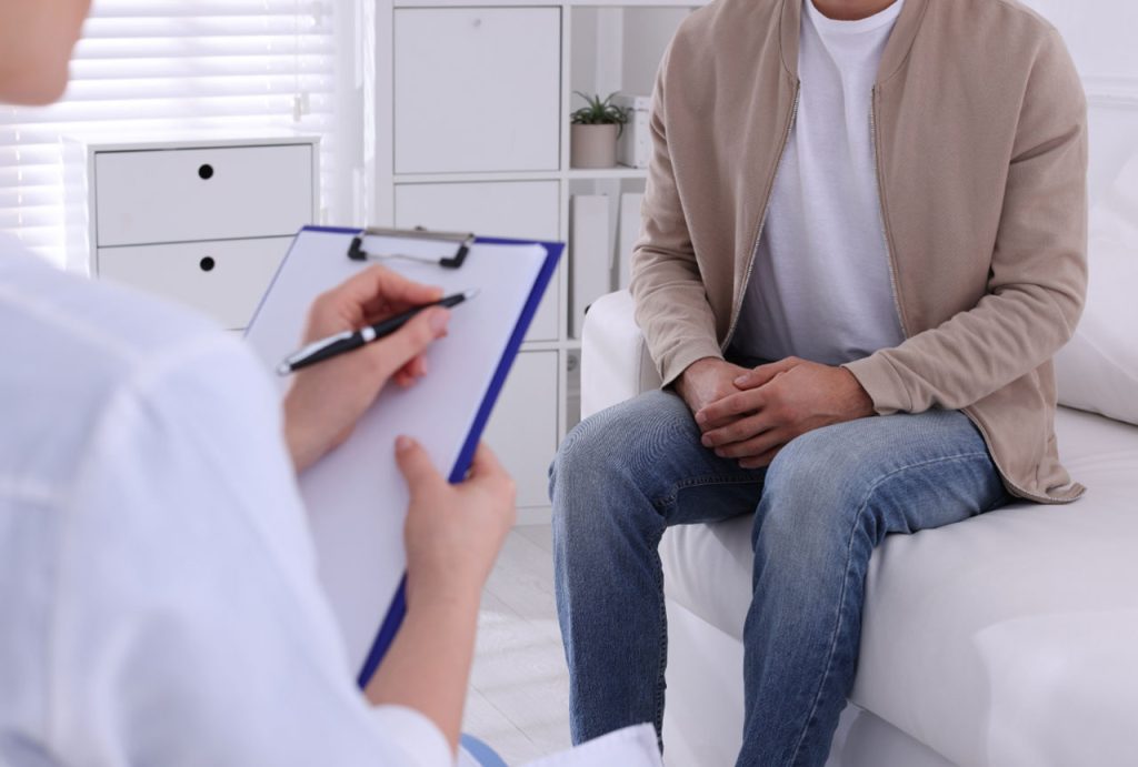 Doctor with clipboard consults a male patient on a white couch, detailing a confidential gay men STD test in Houston.
