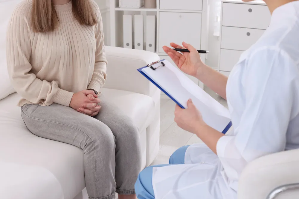 Perspective view of medical professional with clipboard counseling a seated woman. Vital talk on confidential std testing Houston.