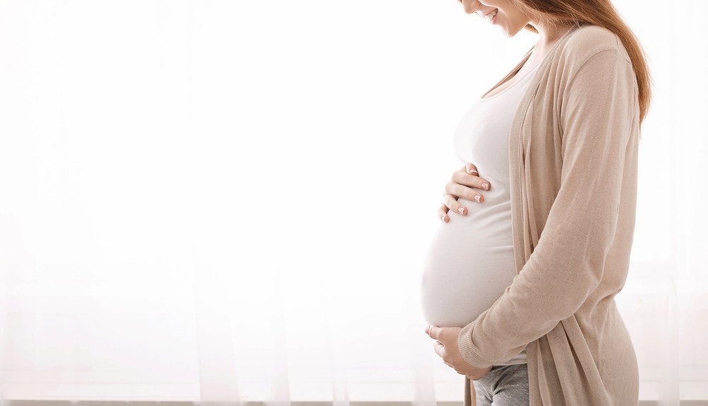 Pregnant woman near window, cradling belly. Ensure health with essential screenings, including cheap sti testing Houston.