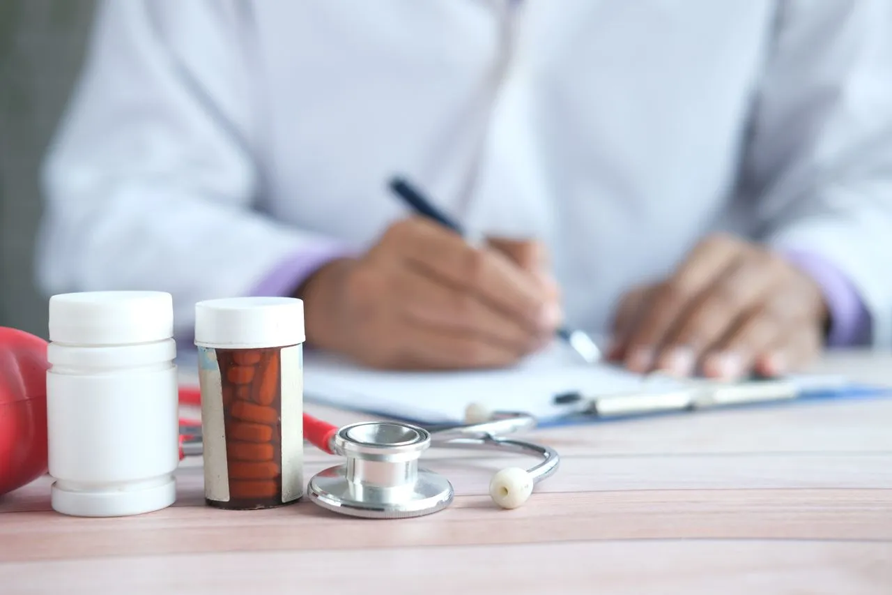 Doctor writing a prescription behind pill bottles and a stethoscope on a desk for Private Pharmacy services.